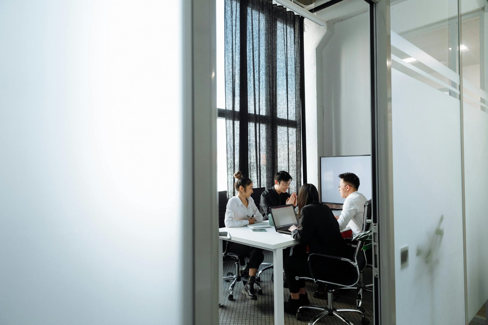 Group collaborating in a well-lit office room with large windows, discussing business strategies.